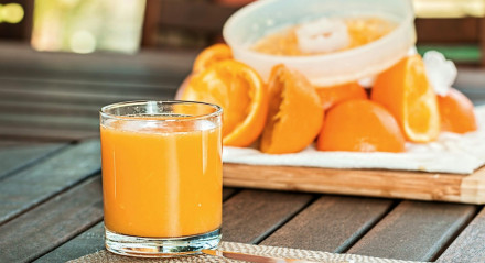 Imagem de um suco de laranja com a fruta em segundo plano