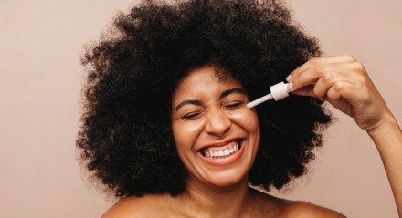 Imagem de mulher aplicando sérum no rosto e sorrindo; skin care