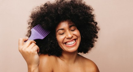 Imagem de mulher de cabelos crespos sorrindo enquanto penteia o cabelo