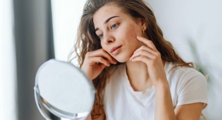 Imagem de mulher jovem se olhando no espelho; skin care