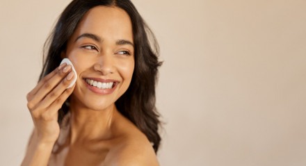 Imagem de mulher sorrindo passando disco de algodão na bochecha; skin care
