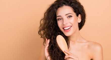 Mulher sorridente enquanto penteia os cabelos com uma escova