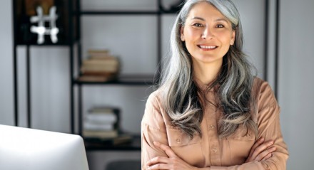 Imagem de mulher com cabelos grisalhos de braços cruzados sorrindo