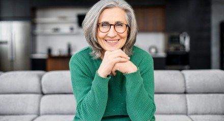 Imagem de mulher com cabelos grisalhos sorrindo, sentada em um sofá
