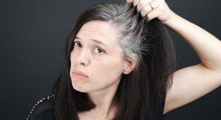 Imagem de mulher observando cabelos grisalhos dela, com semblante de preocupação