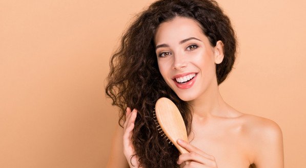 Imagem: Mulher sorridente enquanto penteia os cabelos com uma escova