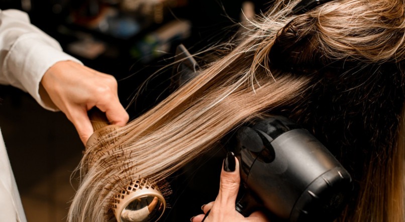 Imagem dos cabelos de uma mulher sendo escovados em um salão de beleza