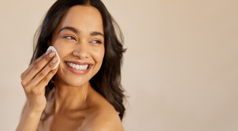 Imagem de mulher sorrindo passando disco de algodão na bochecha; skin care