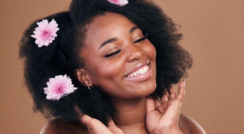 Imagem de mulher com flores no cabelo sorrindo; cabelos crespos; cabelos cacheados