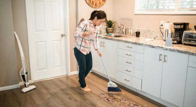 Mulher varrendo o lixo de casa utilizando a vassoura. 