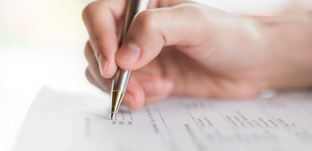 Imagem ilustrativa de uma mão segurando uma caneta sobre um papel; provas do Concurso Nacional Unificado acontecem no início de maio