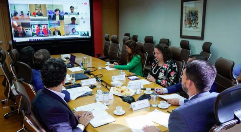 Representantes do Ministério da Cultura do Brasil em mesa de reunião, na tela de uma televisão estão os representantes chineses em chamada de vídeo