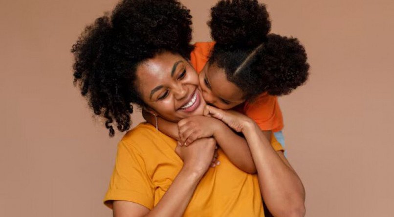 Imagem ilustrativa de uma mãe recebendo carinho da filha; Dia das Mães é celebrado no dia  12 de maio