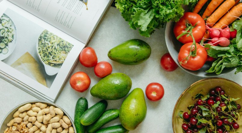 Foto de frutas e legumes espalhados ao lado de um livros de receitas