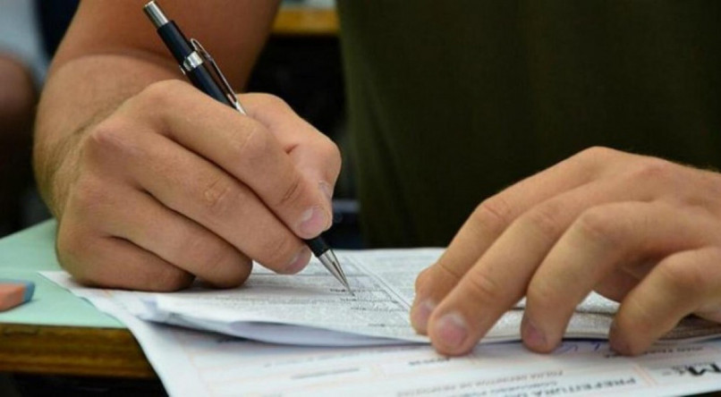 Imagem ilustrativa de uma mão segurando uma caneta sobre uma prova; testes do Concurso Público Nacional Unificado (CPNU) acontecem em maio