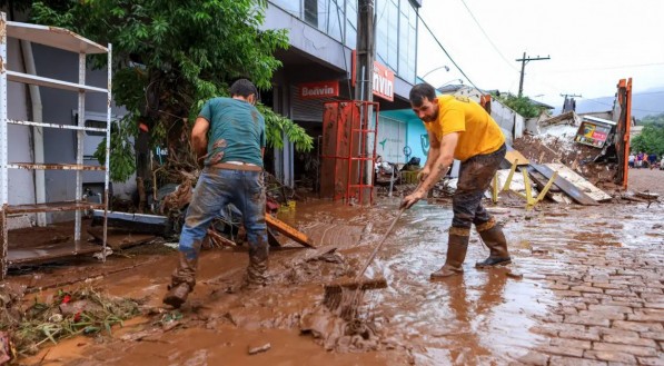 Na imagem, dois homens tentando remover a lama causada pelos temporais no RS