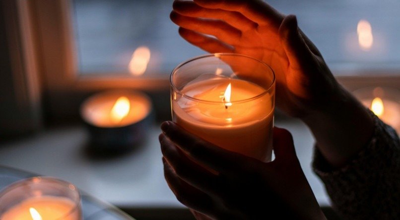 Mãos segurando uma vela e a mantendo acesa.