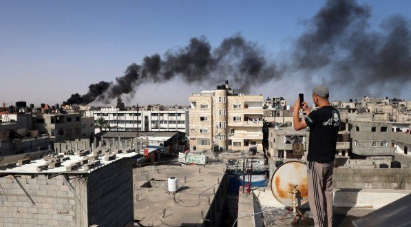 Um homem tira fotos de um telhado enquanto uma fumaça espessa e preta sobe de um incêndio em um prédio em Rafah