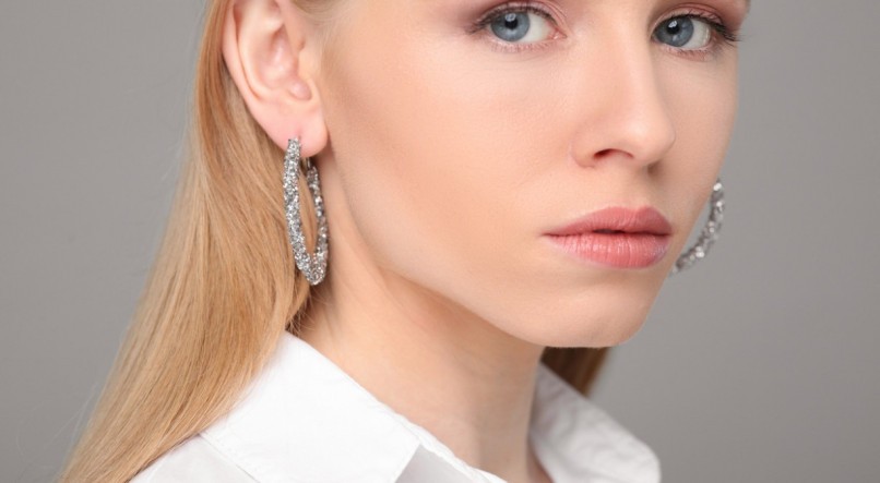 Beautiful young woman with elegant earrings on gray background, closeup