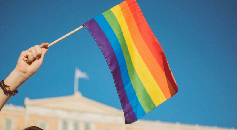 Na imagem, uma pessoa segurando uma bandeira LGBTQIA+