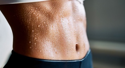 Close up of fit woman torso with sweat on skin after workout. Female with perfect abdomen muscles