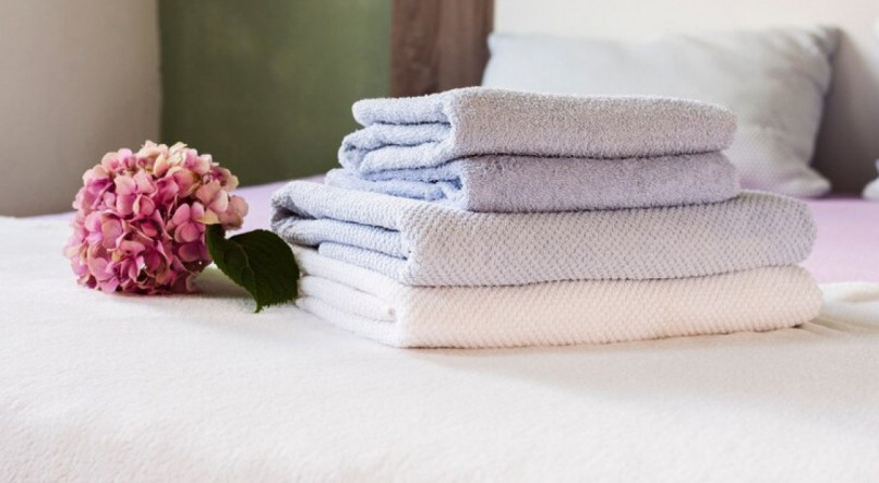 Imagem ilustrativa de toalhas macias e cheirosas dobradas em cima da cama