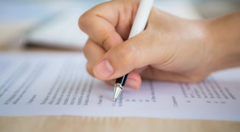 Imagem mostra uma mão segurando uma caneta sobre um papel, ilustrando o CNU - Concurso Nacional Unificado