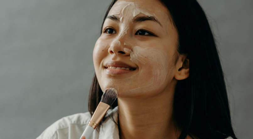 Imagem de mulher passando protetor sola no rosto com pincel.
