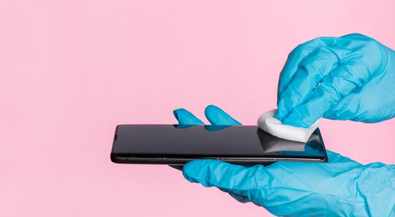 Imagem ilustrativa de uma mão com luvas limpando a tela de um celular