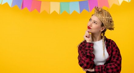 Garota loira no festival brasileiro de chap&eacute;u de palha com bandeiras coloridas pensando com maquiagem junina
