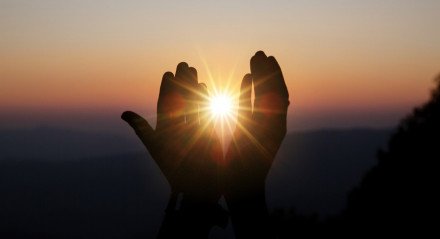 Imagem ilustrativa de mãos erguidas diante de um pôr do sol para mensagem de gratidão