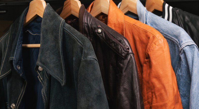 Various vintage suede leather and jeans jackets on hanger rack in a used goods store. Thrifting and sustainability in clothing concept