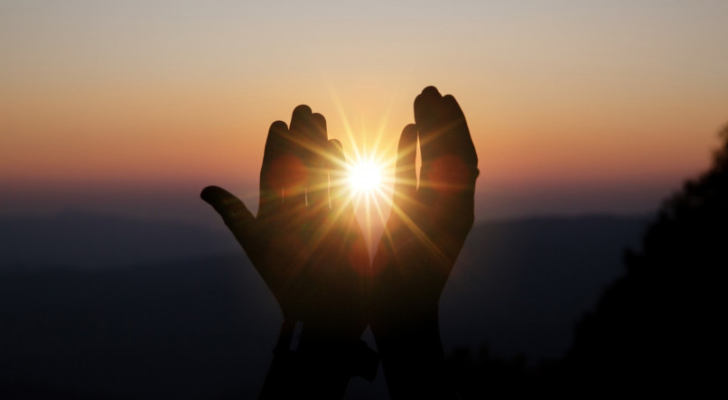 Imagem ilustrativa de mãos erguidas diante de um pôr do sol para mensagem de gratidão