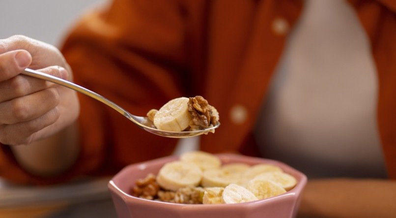 Pessoa comendo refeição à base de banana e granola. 