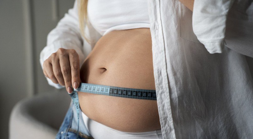 Mulher medindo circunferência abdominal com fita métrica. 