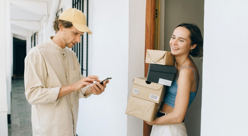 Imagem ilustrativa de entregador fazendo uma entrega para uma mulher, que está segurando caixas
