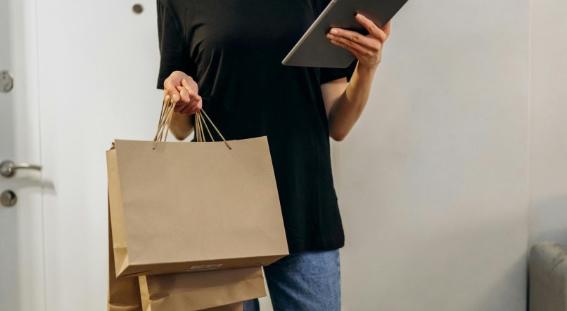 Imagem ilustrativa de uma pessoa segurando sacolas de compras e um tablet