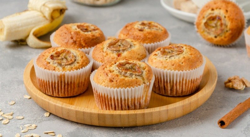 Muffins de banana com aveia, nozes e canela em um prato de madeira no fundo de concreto cinza. Sobremesa saudável.

