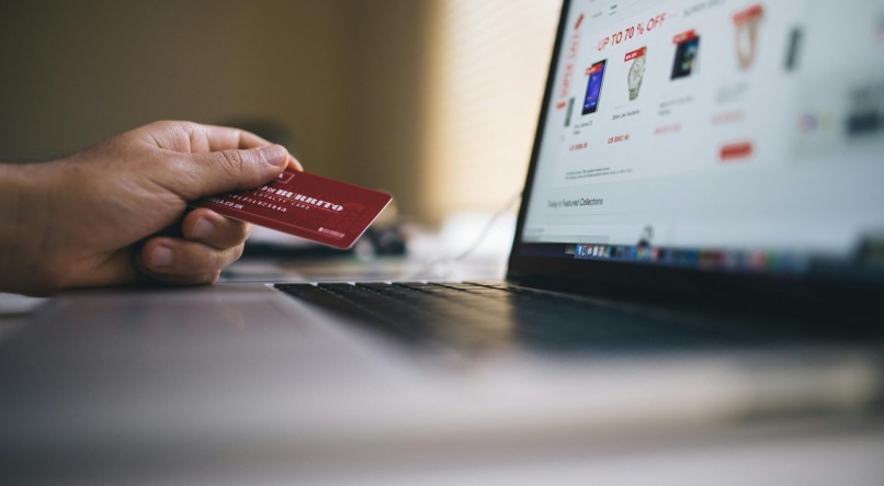Imagem ilustrativa de uma pessoa segurando um cartão de crédito e olhando para um e-commerce
