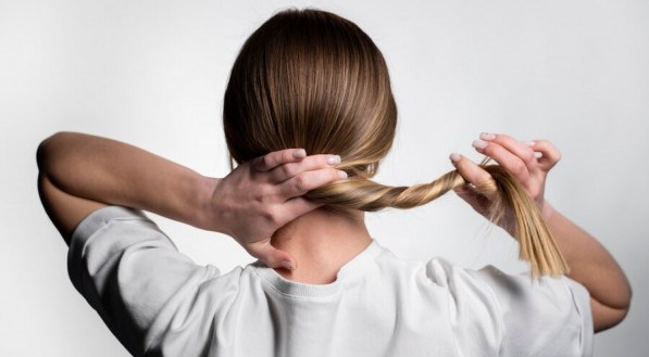 Mulher de costas segurando o cabelo com as duas mãos