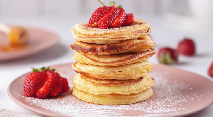 Freshly baked pancakes with strawberries on a natural wood background