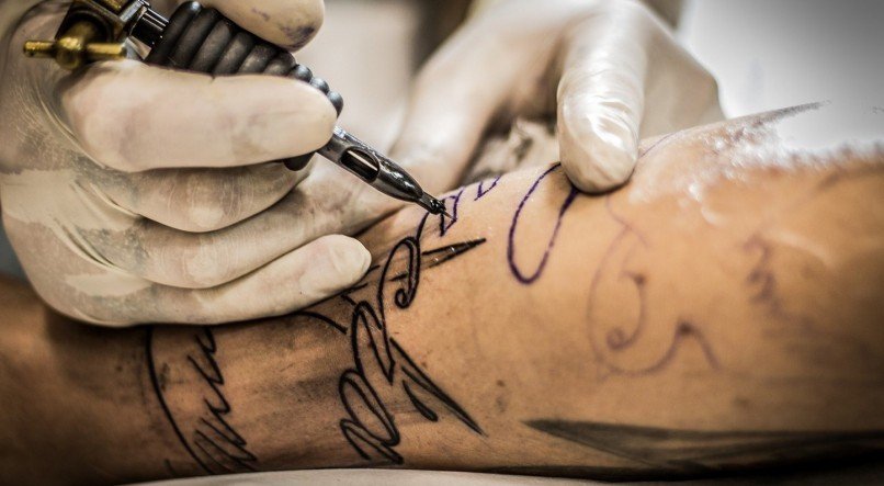 Profissional realizando tatuagem na região do braço. 