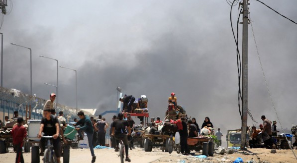 Os palestinos fogem com os seus pertences enquanto a fumaça sobe ao fundo, na área de Tel al-Sultan, em Rafah, no sul da Faixa de Gaza
