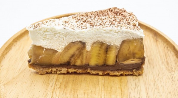 Torta de Banoffee, chantilly e banana na placa de madeira isolar fundo branco
