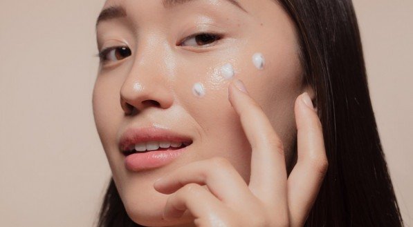 Close up of a young woman applying moisturizer to her face. Asian woman looking happy while following skincare regime.