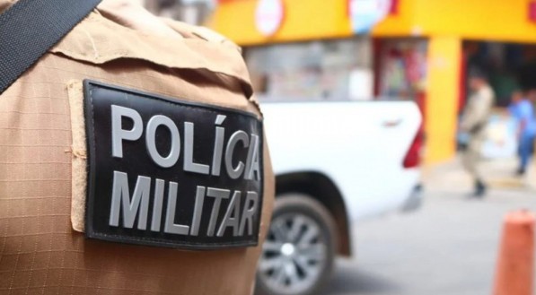 Imagem mostra em primeiro plano a farda de um PM escrito "Polícia Militar"