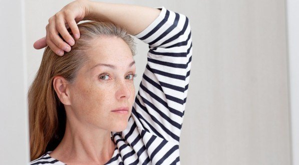 Imagem de uma mulher olhando para o cabelo branco no reflexo do espelho