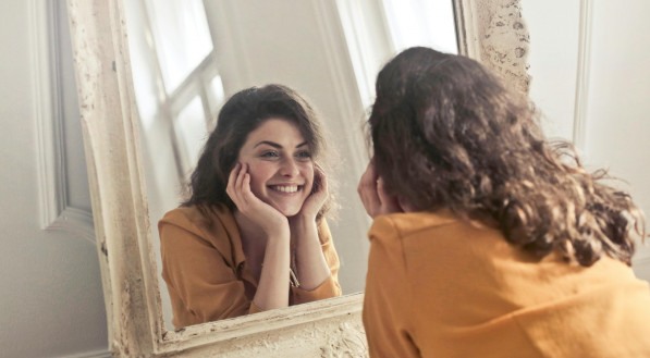 Imagem ilustrativa de uma mulher feliz sorrindo de frente ao espelho
