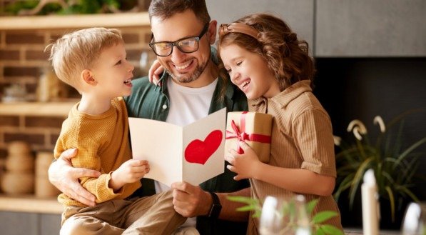 We love you, dad. Young happy father getting congratulations on Fathers Day from two excited kids at home, son and daughter, smiling children giving daddy handmade postcard and wrapped gift box
