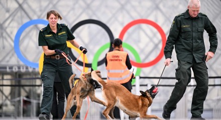 Agentes de segurança dos Robezsardze, guardas de fronteira da Letônia, patrulham com cães em frente à Pirâmide do Louvre, projetada pelo arquiteto sino-americano Ieoh Ming Pei, poucas horas antes do início da cerimônia de abertura dos Jogos Olímpicos de Paris 2024 em Paris em 26 de julho de 2024
